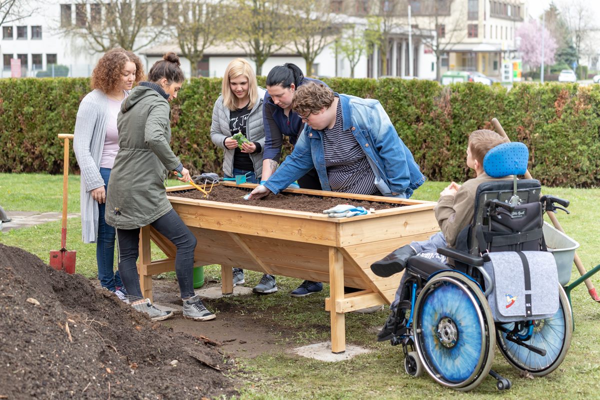 dm Mitarbeiter bei der Gartenarbeit mit den Klienten der Tagesstätte „Die Vier Jahreszeiten“